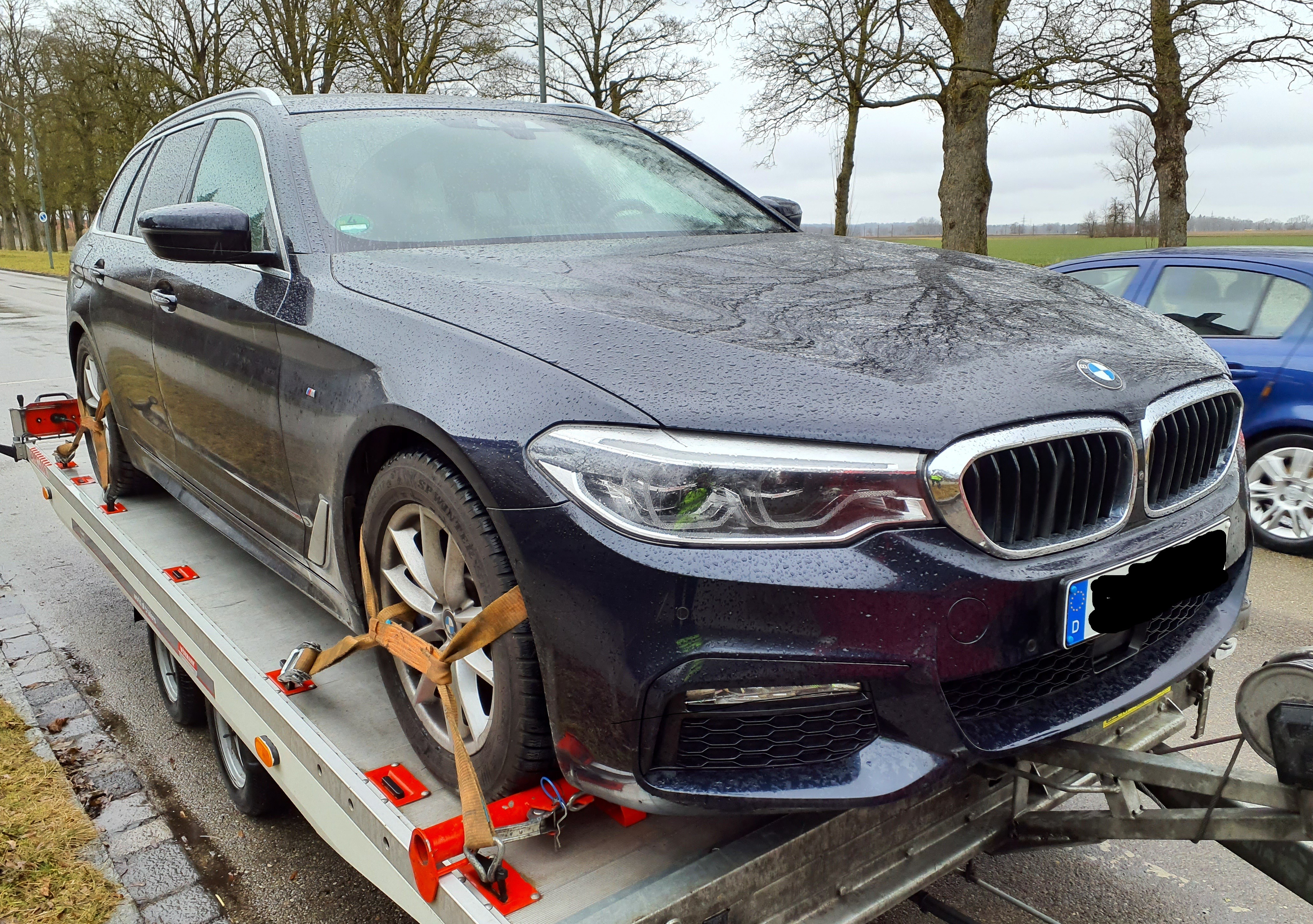 Schwarzer BMW PKW transportiert auf einem Anhänger, an einem regnerischem Tag.